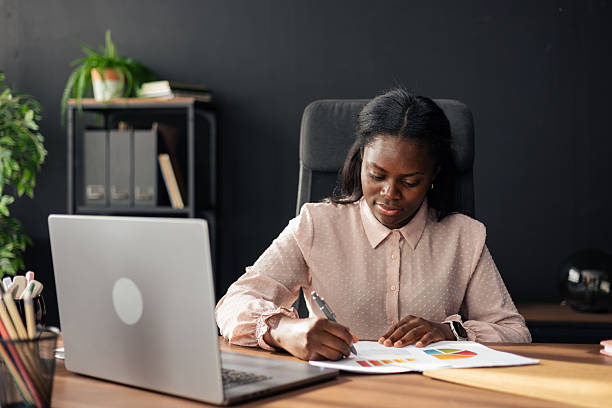istock Black businesswoman analyzing graphs and writing report in office 2238943363