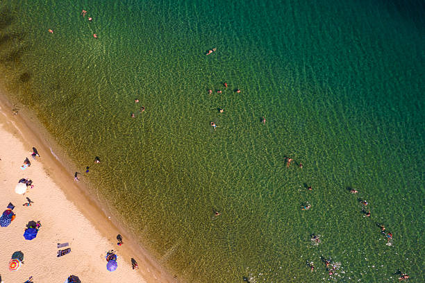 Aerial view of people swimming in clear turquoise water and relaxing on a sandy beach