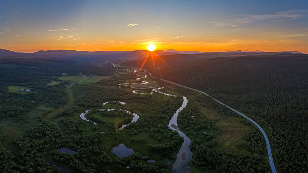 A breathtaking aerial view of a the winding river of Ljusnan meandering through a lush green forest and open valley at sunset. The golden light reflects on the water’s curves, creating a serene and picturesque landscape. Captured in Bruksvallarna, Härjedalen, Sweden, this scenic panorama highlights the beauty of untouched nature and the tranquility of golden hour in the wilderness.
