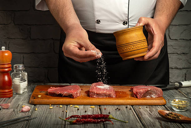 istock In a rustic kitchen, a chef seasons fresh cuts of steak with salt from a wooden container while surrounded by various spices and tools 2238955198