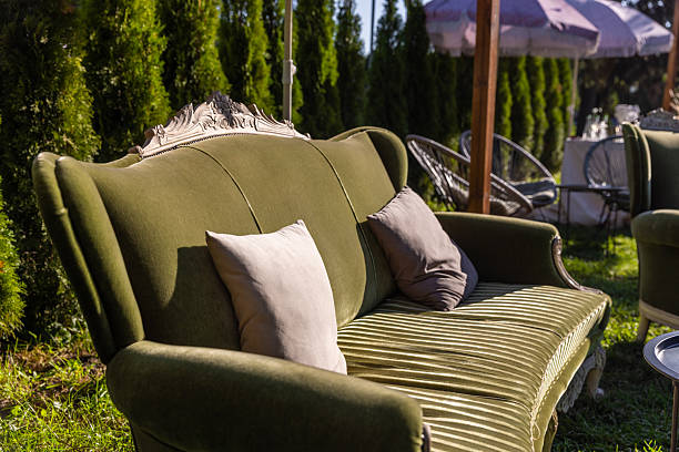 Three brown sofa seats are set up on green artificial grass that is spread out on the concrete floor of the foyer, providing a waiting area for performances near a field in the Thai countryside.