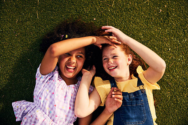 istock Overhead view of two diverse best friends laughing and touching each other while lying on green grass at school 2238960037