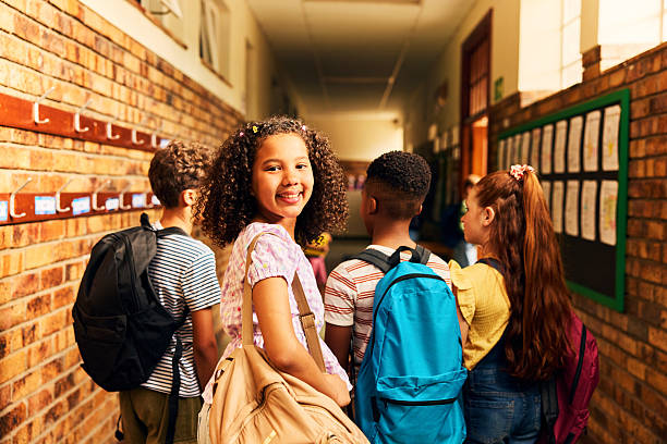 istock Smiling girl  with curly hair looking over her shoulder while walking with classmates through school hallway 2238960088