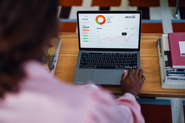 A focused individual uses a laptop on a wooden desk displaying a colorful business dashboard with charts and graphs, conveying analytics, productivity, and data-driven decision making in a modern setting.