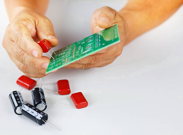 istock The image shows a red electronic component, likely a capacitor or resistor, being held in hand for assembly on a green printed circuit board (PCB). 2238963226