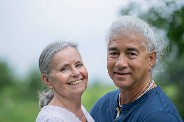 A smiling older couple outdoors in a leafy setting, enjoying a peaceful walk together. The mixed-heritage pair exudes warmth and connection, capturing everyday happiness in a natural, relaxed moment.