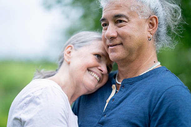 Two senior companions share a warm, smiling moment outdoors, leaning close in a peaceful park. A tender portrait of companionship, comfort, and enduring connection in nature.