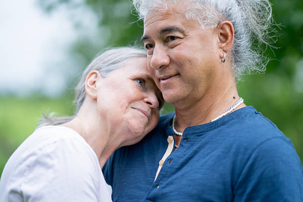 A warm, affectionate moment between an older couple outdoors. They lean into each other with gentle smiles, conveying love, companionship, and comfort in a peaceful natural setting.