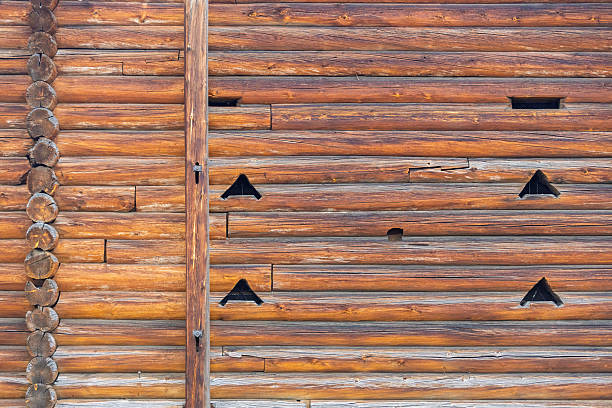 An old wooden barn wall made of round logs with ventilation holes. Textured background with copy space. Russian architecture.