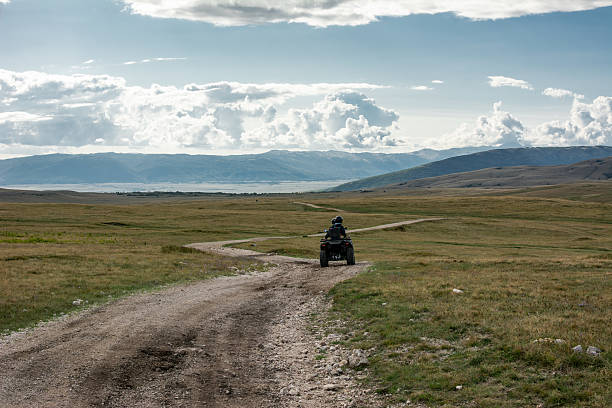 Two people ride ATVs across a mountainous karst plateau on a partly cloudy autumn day