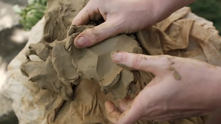 Closeup horizontal video of working with wet clay. Hands separate small lumps of clay, kneading the clay for handmade craft pottery.