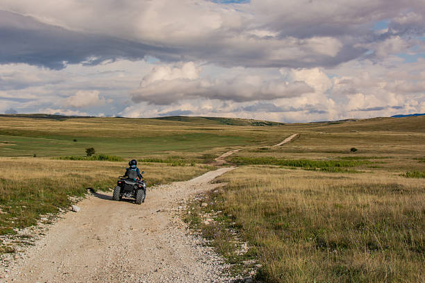 Two people ride ATVs across a mountainous karst plateau on a partly cloudy autumn day