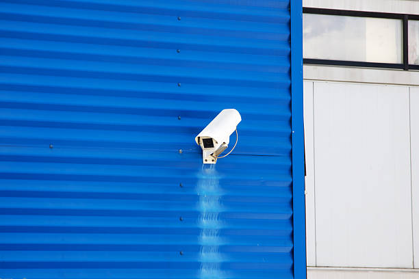 A security camera is mounted on the side of a blue colored building