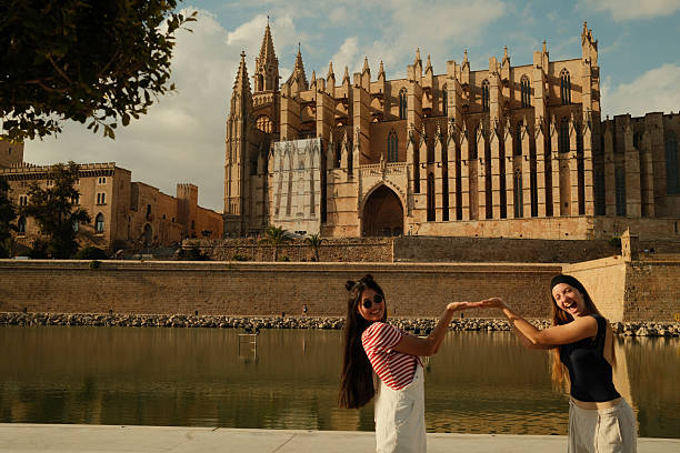 Two young women having fun manipulating perspective with Palma Cathedral in Spain, enjoying their European travel and friendship