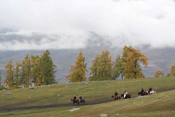 This photo shows a group of people riding horses across autumn grasslands, with golden trees and a vast sky in the background. The scene highlights cultural experience, outdoor lifestyle, and the beauty of nature, suitable for travel and adventure themes.