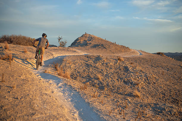 a mountain biker speeds by on a desert meadow trail as the sunset light illuminates the horizon of dramatic sky at sunset. horizontal wide angle composition with copy space in sky.