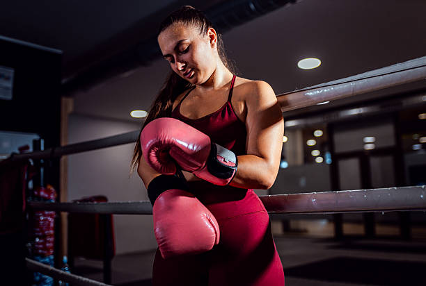 istock Confident female boxer putting gloves on hands preparing for training in boxing ring. 2238984437