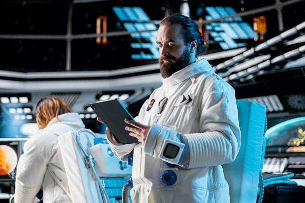 Astronaut wearing spacesuit inside futuristic spacecraft monitoring mission data on tablet screen. Spaceman wearing equipment helmet prepares for space travel operations, reading data on device