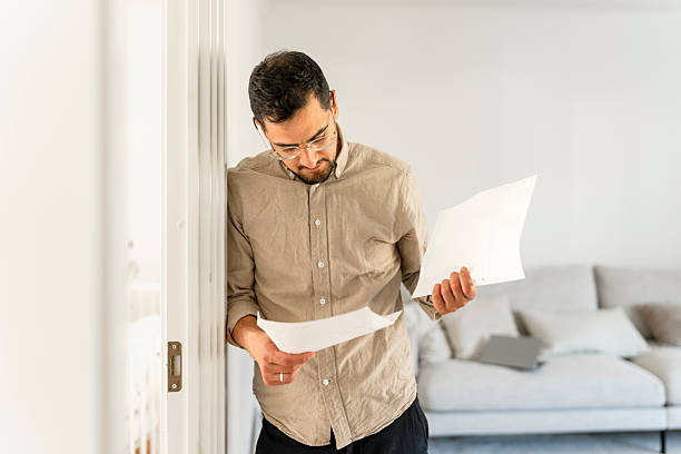 istock A man reviews financial documents at home, leaning on a doorframe while studying papers 2238986027