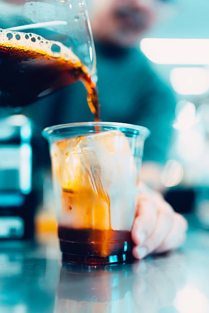 Pouring espresso shot into iced coffee in transparent cup with ice