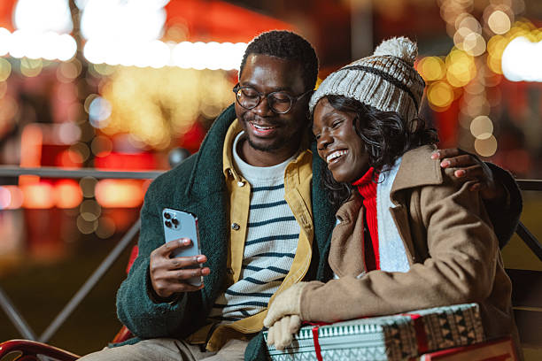 istock Happy couple enjoying Christmas festive lights outdoors and using a smartphone 2238990077