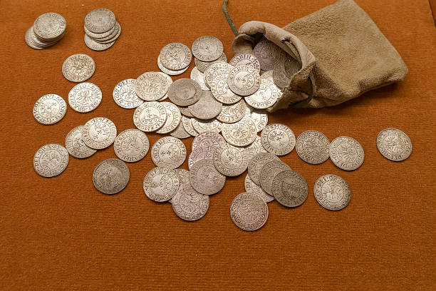 istock Collection of ancient silver coins spilled from a small pouch on an orange cloth surface 2238990514