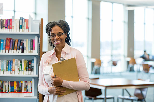 istock Smiling librarian holding clipboard near bookshelves in modern library setting 2238997704