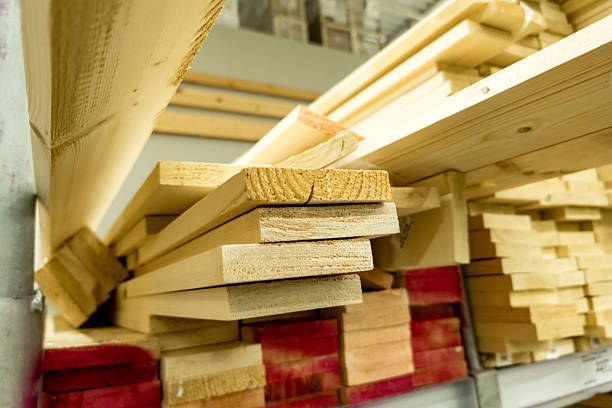 A collection of cut wooden planks is stacked neatly in a workshop, showcasing various sizes and types of wood. Natural light brightens the space, enhancing the raw materials.