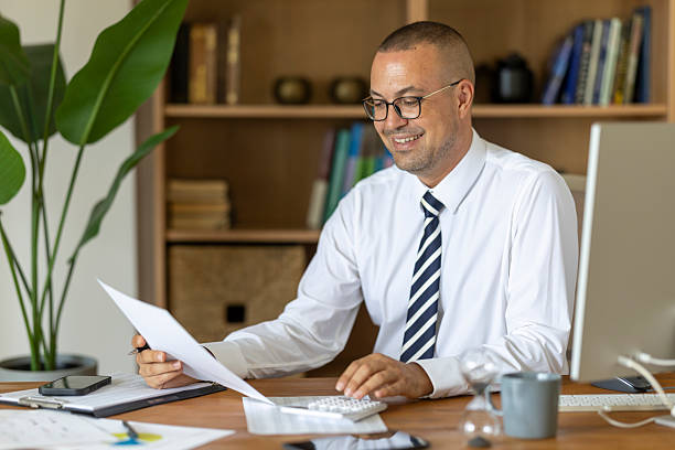 Businessman smiling, calculating finances and doing paperwork in home office