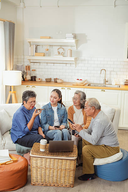 smart daughter teaches senior parents and friend voice activated AI assistant technology on smartphone, demonstrating hands free virtual chatbot for simplified daily tasks and big data applications at home living room