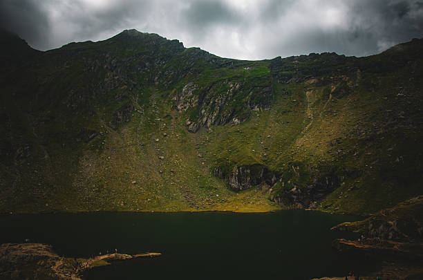 istock Dramatic Glacial Lake and Rocky Mountain Slope Under Dark Storm Clouds 2239027946