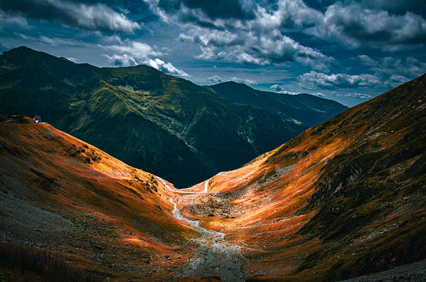 Mountain landscape featuring sunlit valley surrounded by dense green forest and tall peaks with dramatic sunlight streaming through clouds illuminating slopes and treetops
