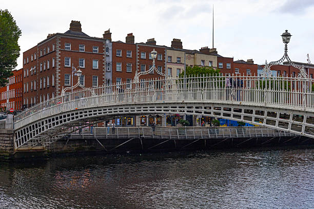 Dublin, Ireland - July 31, 2025: The Ha' penny Bridge, a white, arched, cast iron, pedestrian bridge, spans the calm River Liffey on a summer day in Dublin, Ireland.