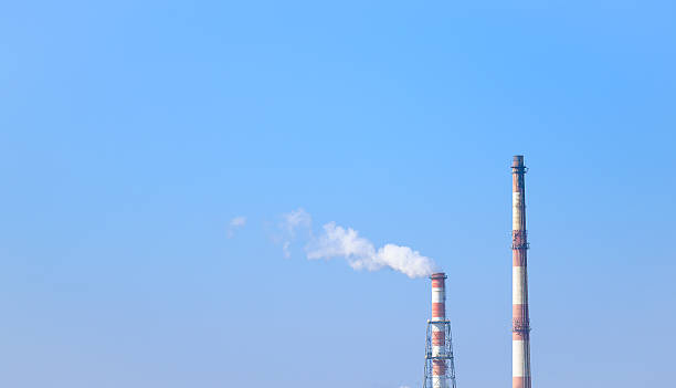 Factory chimneys releasing smoke into clear blue sky. Symbol of industrial production, pollution, and energy manufacturing in modern industry. Environmental impact and air quality concept.