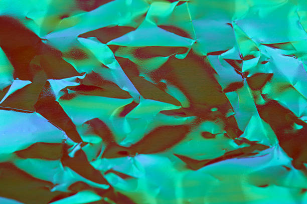Crumpled wrapping paper in shimmering turquoise and pink, forming abstract textured surface with dynamic folds