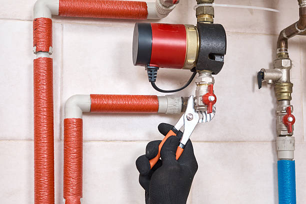 Plumber hands in protective gloves installing and connecting a water circulation pump and pipes for a domestic heating system