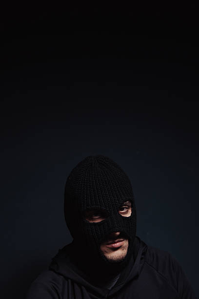 Unrecognizable cyber criminal or computer hacker wearing black hooded jacket, low key portrait, selective focus