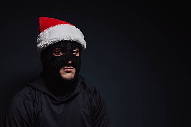 istock masked robber with Christmas hat on a black background 2239039583