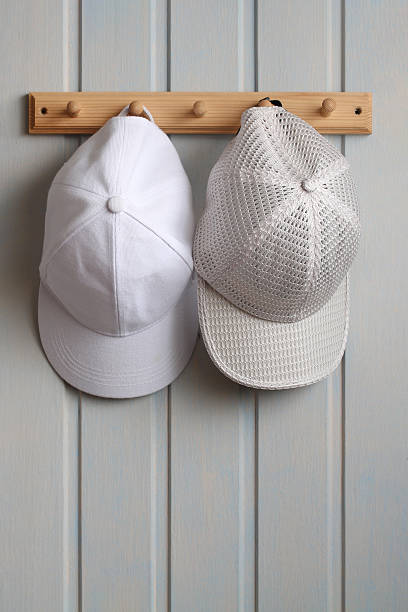 istock White baseball caps hanging on wooden hook rack 2239044505