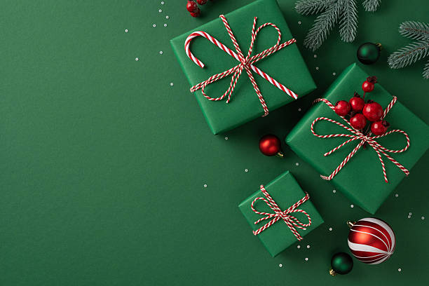 istock Green gift boxes tied with red and white string sit against a festive backdrop with berries and ornaments, evoking Christmas and New Year mood, gift giving, decoration, and seasonal joy 2239048270