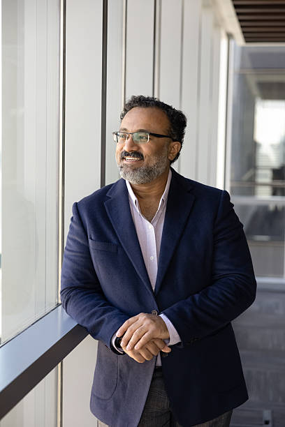 istock Cheerful positive successful senior Indian executive man standing at window 2239050041