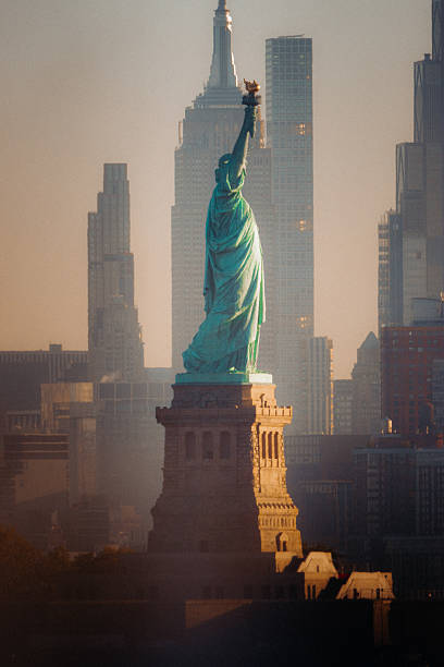 The Statue of Liberty and Empire State Building align at sunrise from New Jersey