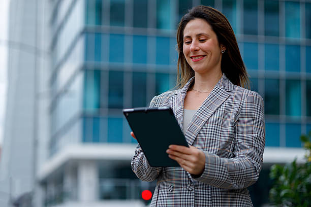 istock Businesswoman standing outdoors in front of an office building, smiling while using a digital tablet for work 2239055709