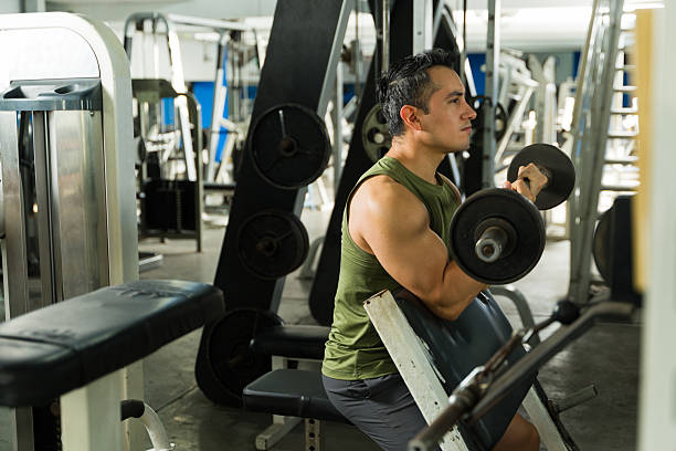 Hispanic male athlete performing preacher curl with barbell on bench in gym, focused on building biceps and strength during workout