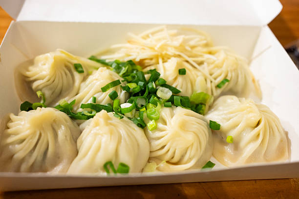 Asian noodles cooked with vegetables in a white bowl. A dumpling is placed on top of the dish