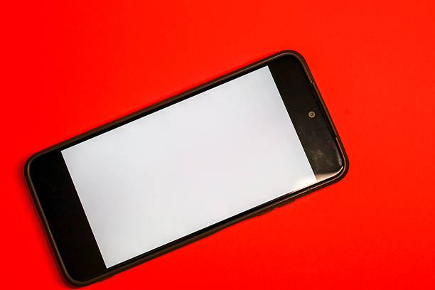 ​A smartphone with a clean white screen is positioned diagonally on a vivid red background, creating a striking visual contrast. This digital mockup is ideal for presenting a mobile interface, applications, or advertisement messages on a bright backdrop.