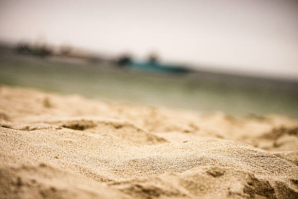 Detailed view of golden sand grains with soft focus on the seashore in the background. Minimal beach scene, perfect for summer, holiday, relaxation, nature and background concepts.