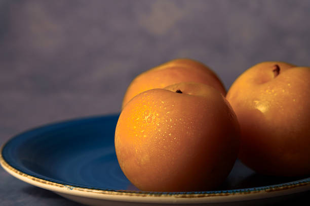 Ripe yellow plums with water drops resting on a contrasting blue ceramic plate in soft light