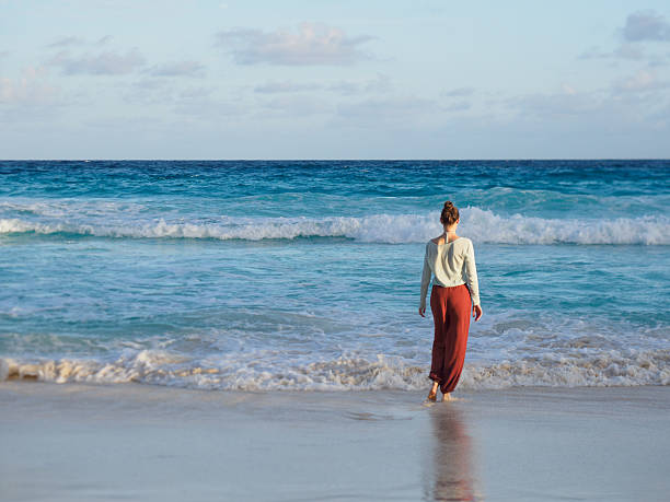 Cute woman walking on stunning white sand beach with palm trees and rocks in the background. Beautiful views and sights of Seychelles. Clear, warm sunlight. Outdoor. Concept of leisure and travel
