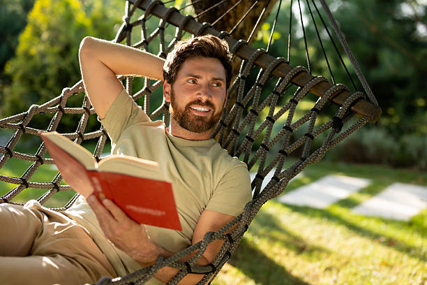 istock Caucasian bearded young man lying in hammock with a book in hands 2239108279
